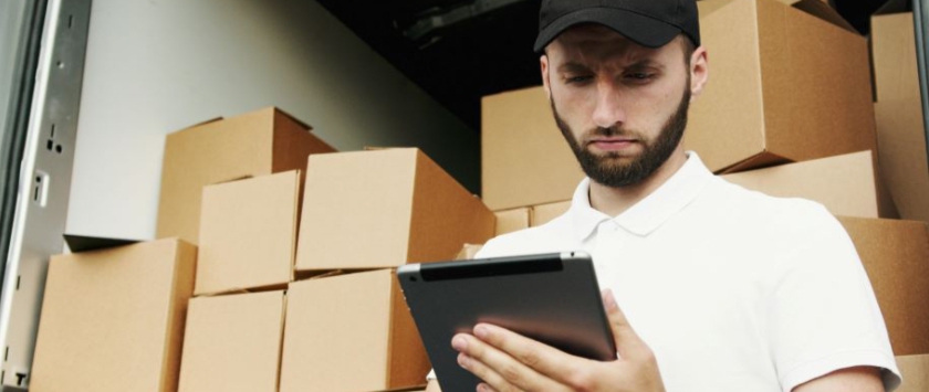 A man in a white shirt moving boxes and using his tablet