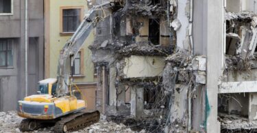 An excavator actively demolishing a historic building, highlighting the importance of careful and strategic dismantling to preserve architectural elements and minimise environmental impact, as part of responsible urban redevelopment.