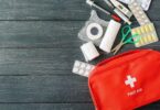 Essential first aid supplies including bandages, scissors, tape, and medications displayed alongside a red first aid kit on a wooden background