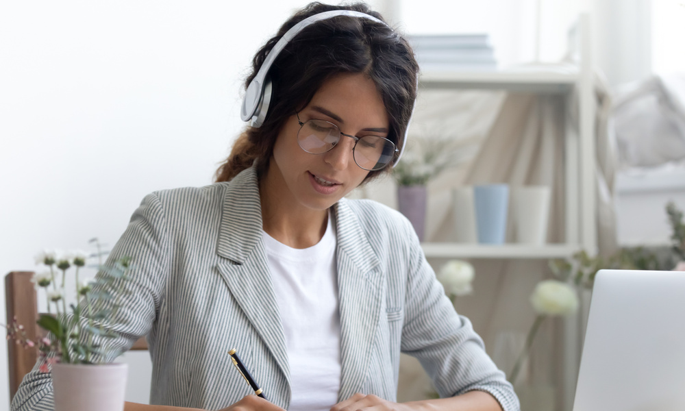 A woman working on her tasks while wearing noise-canceling headphones. She writes something down in a notebook
