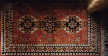 An aerial view of a patterned red rug on a dark wood floor in a room with low lighting.