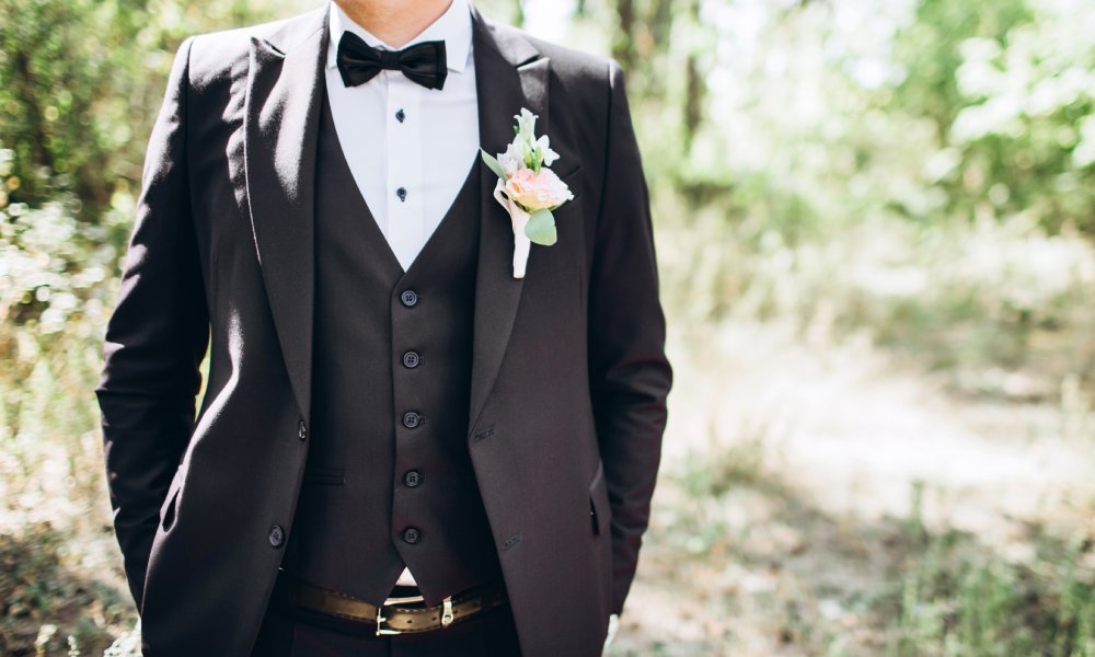 A man in a white shirt and a black suit with a pink and green boutonniere pinned to the lapel of his jacket.