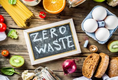 Various fresh foods surround a chalkboard reading “ZERO WASTE” in all caps, including eggs, bread, and produce.