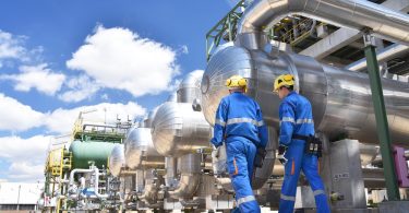 Two workers in an industrial plant for the production and processing of oil. They're wearing blue protective suits.