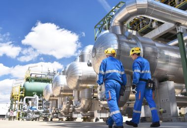 Two workers in an industrial plant for the production and processing of oil. They're wearing blue protective suits.
