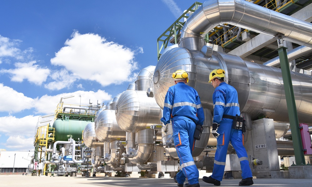 Two workers in an industrial plant for the production and processing of oil. They're wearing blue protective suits.