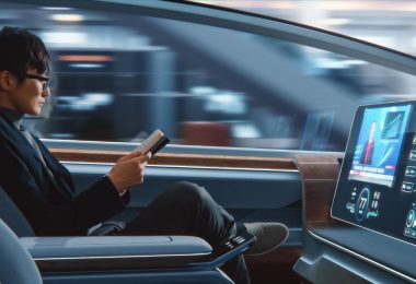 A passenger in an autonomous vehicle, reading a book as the car drives for him. He's in business casual attire.