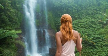 Female traveler admiring a hidden waterfall on a tropical island surrounded by lush greenery.