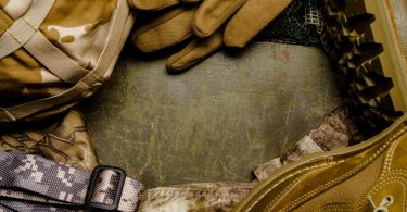 Military supplies on a scratched green table. The supplies include gloves, boots, a strap, and a bag.