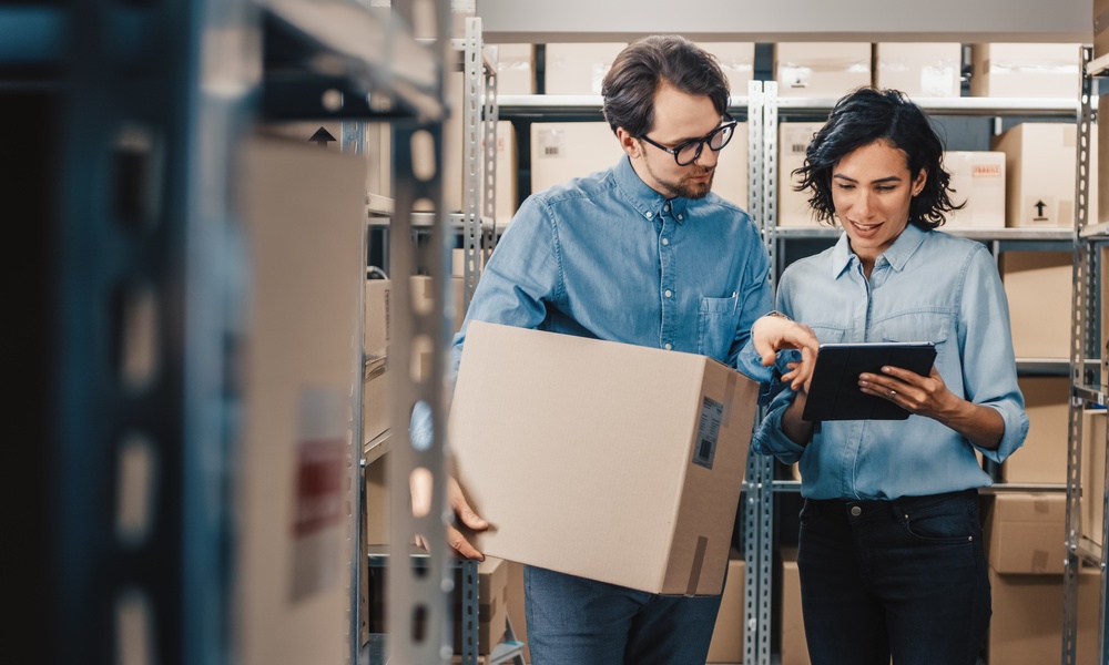 A man and a woman are standing next to each other. The woman is holding a tablet and they’re both looking at it.