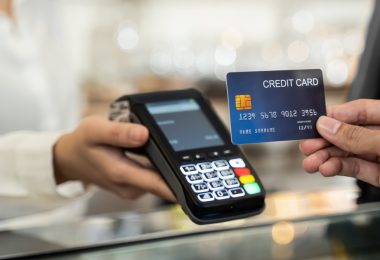 An individual holding a blue credit card near a payment terminal as a cashier processes a transaction.