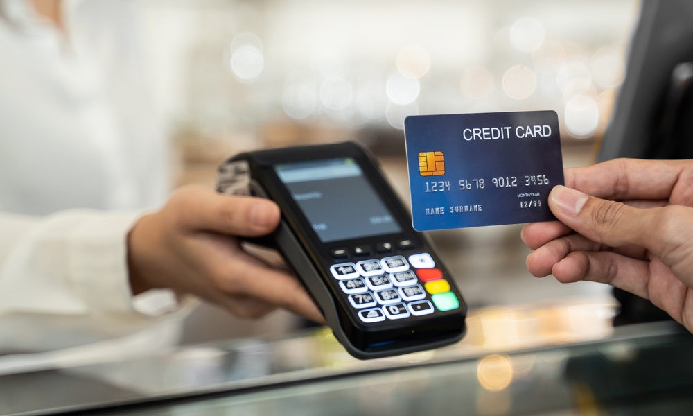 An individual holding a blue credit card near a payment terminal as a cashier processes a transaction.