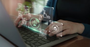 A close-up of a person typing on a laptop keyboard with various abstract business symbols floating above.