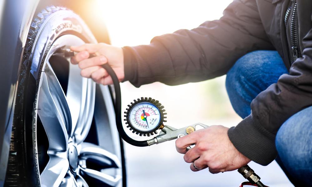 A person wearing a black jacket and jeans checks tire pressure using a gauge connected to the valve stem.