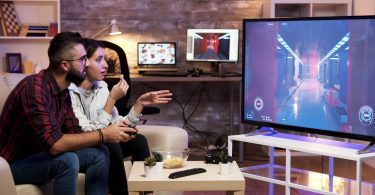 Man playing video games on TV while sitting on couch with girlfriend nearby