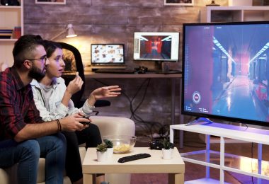Man playing video games on TV while sitting on couch with girlfriend nearby