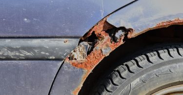 Sunlight shining down onto a rusty blue car parked outside. Rust causes the wheel well to turn orange and break apart.