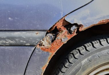 Sunlight shining down onto a rusty blue car parked outside. Rust causes the wheel well to turn orange and break apart.
