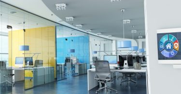 A close-up on a control panel on the wall leading into an office space with several desks and room spaces.
