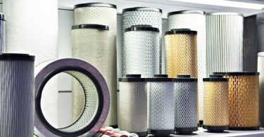 An assortment of industrial air filters of different sizes, colors, and materials arranged on a white shelf.