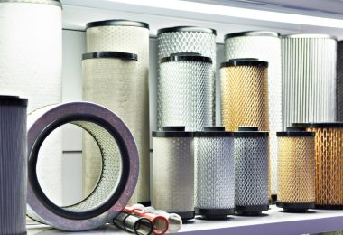 An assortment of industrial air filters of different sizes, colors, and materials arranged on a white shelf.