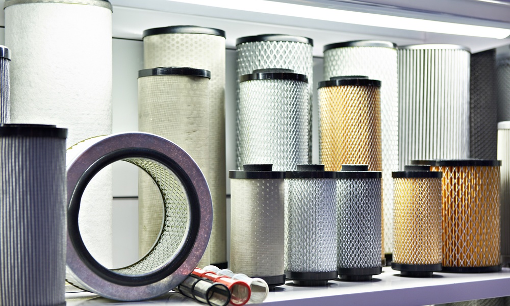 An assortment of industrial air filters of different sizes, colors, and materials arranged on a white shelf.