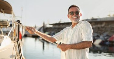 A joyful boat owner standing on a dock and holding a thick white rope leading up to the edge of their white water vessel.