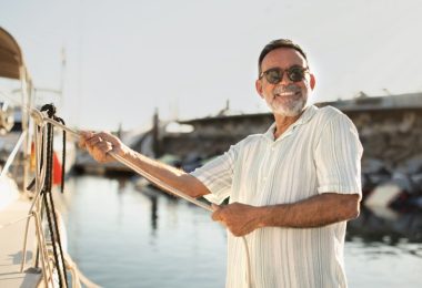 A joyful boat owner standing on a dock and holding a thick white rope leading up to the edge of their white water vessel.