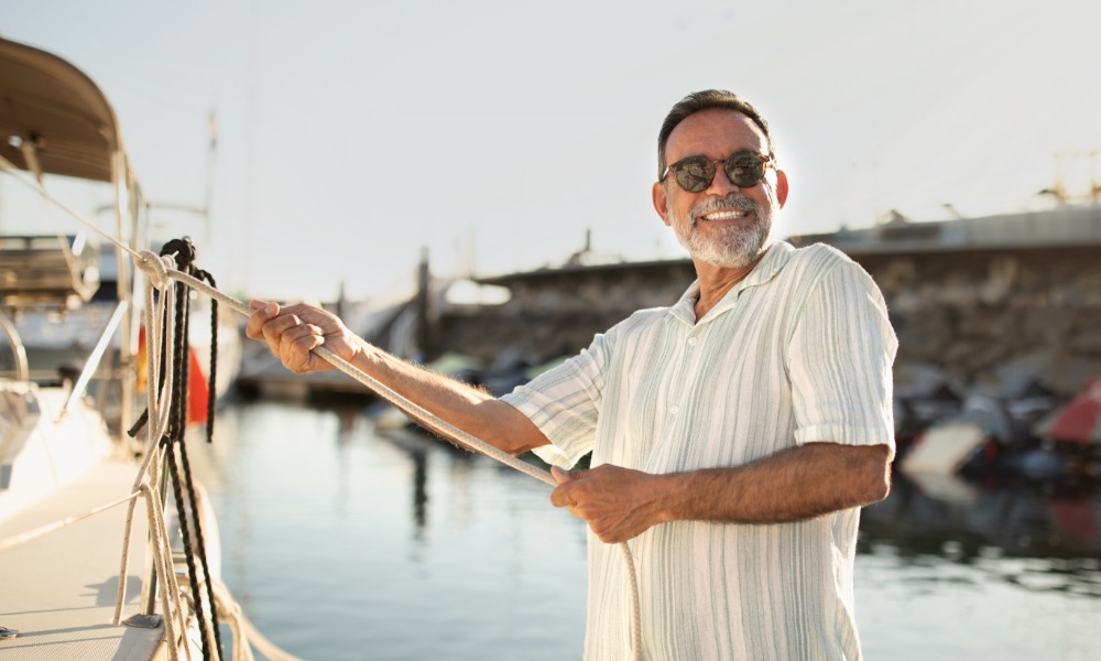 A joyful boat owner standing on a dock and holding a thick white rope leading up to the edge of their white water vessel.