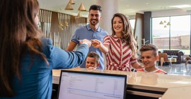 Family checks into a modern hotel as a smiling front desk receptionist hands over a key card in a bright, welcoming lobby.