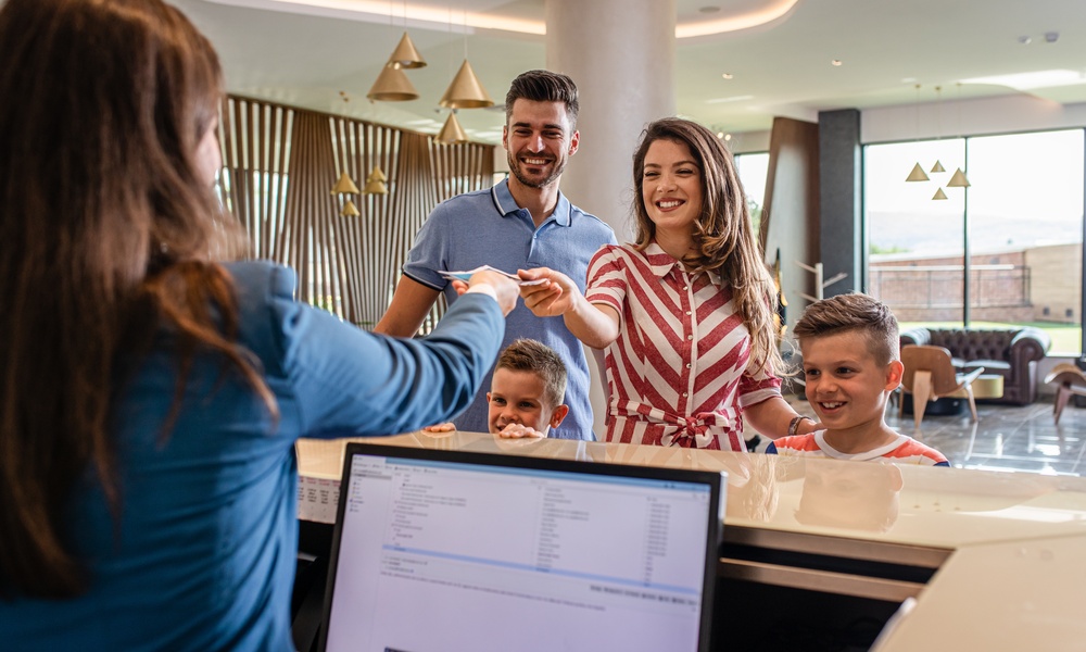 Family checks into a modern hotel as a smiling front desk receptionist hands over a key card in a bright, welcoming lobby.