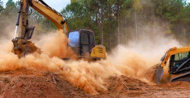 A close-up of an excavator and a skid loader with a bucket attachment kicking up dirt while digging at a development site.
