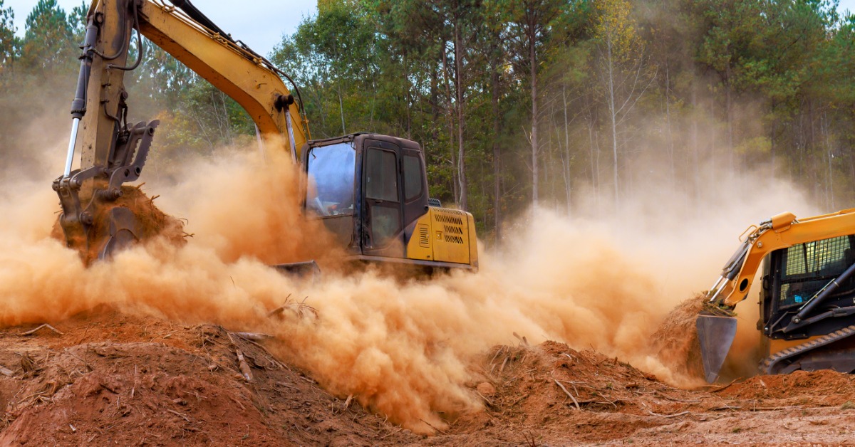 A close-up of an excavator and a skid loader with a bucket attachment kicking up dirt while digging at a development site.