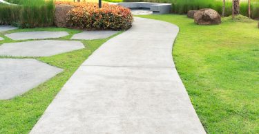A freshly groomed sidewalk outside of a commercial property. The sidewalk is surrounded by green grass.