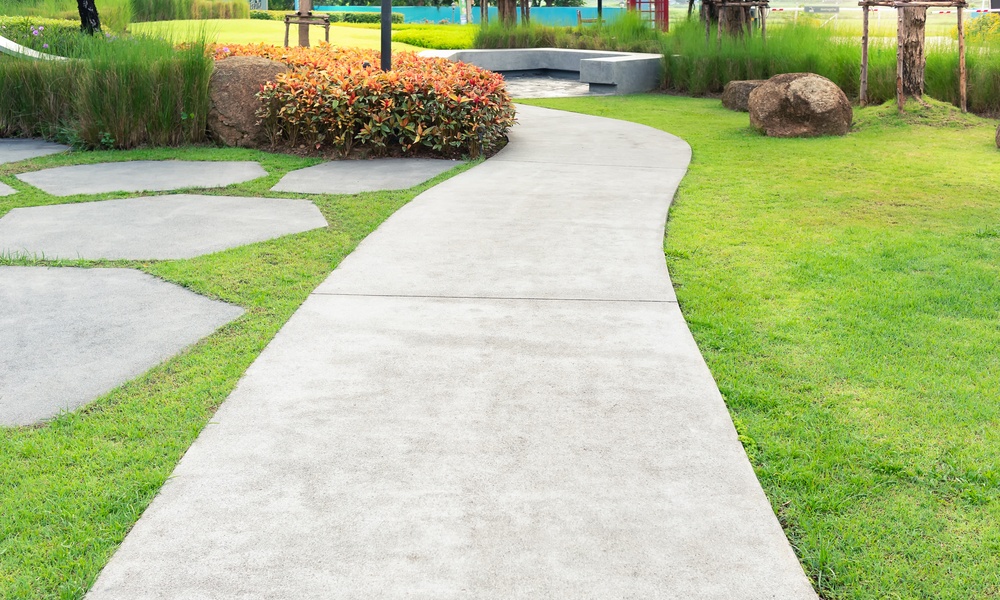 A freshly groomed sidewalk outside of a commercial property. The sidewalk is surrounded by green grass.