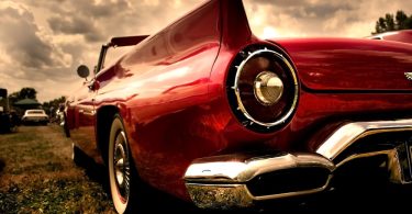 Low-angle view of a red classic convertible with chrome bumper parked outside beneath dramatic cloudy skies.