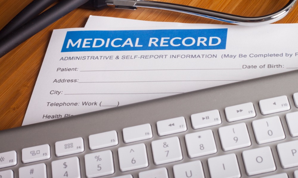 A stethoscope and pen resting on health insurance paperwork and a medical record folder on a desk with white paper beneath.