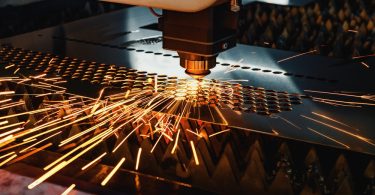 A high-precision CNC machine uses a laser to cut holes in a metal sheet. It creates sparks as it works.