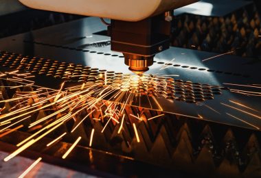 A high-precision CNC machine uses a laser to cut holes in a metal sheet. It creates sparks as it works.
