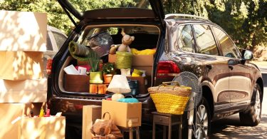 A rear view of a black SUV with its hatchback open and its trunk filled with boxes and items, with more boxes nearby.