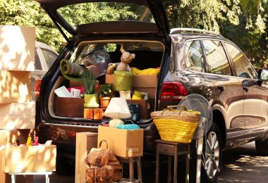 A rear view of a black SUV with its hatchback open and its trunk filled with boxes and items, with more boxes nearby.