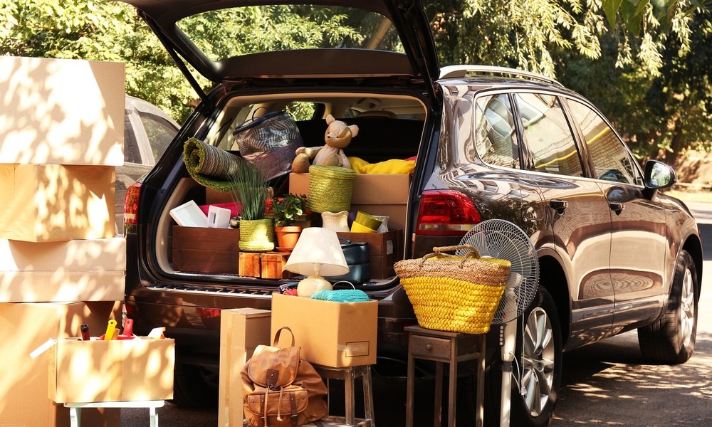 A rear view of a black SUV with its hatchback open and its trunk filled with boxes and items, with more boxes nearby.