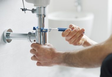 A man is kneeling next to a sink. He’s using a wrench to tighten a connection on the underside plumbing.