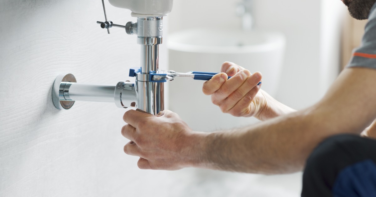 A man is kneeling next to a sink. He’s using a wrench to tighten a connection on the underside plumbing.