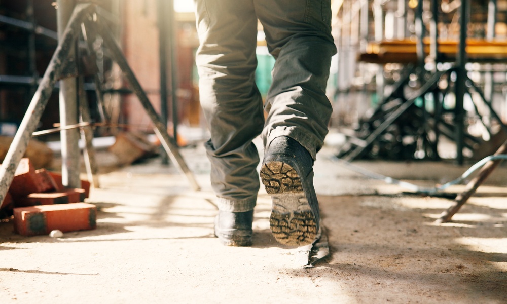 Low-angle view of a person's boots as they walk through a construction site. Bricks and scaffolding are visible.