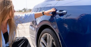 A woman with long hair checking the damage on her vehicle's rear door. There are minor dents near the door handle.