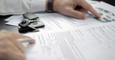 Close-up of car keys on documents while a person reviews paperwork featuring printed currency illustrations.