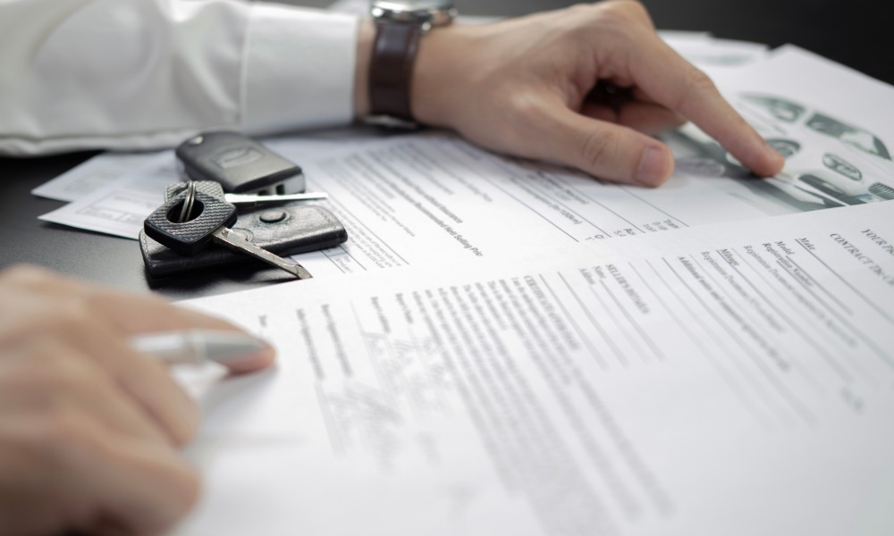 Close-up of car keys on documents while a person reviews paperwork featuring printed currency illustrations.