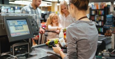 Two parents and their child stand in front of a convenience store cash register while an employee scans a product.