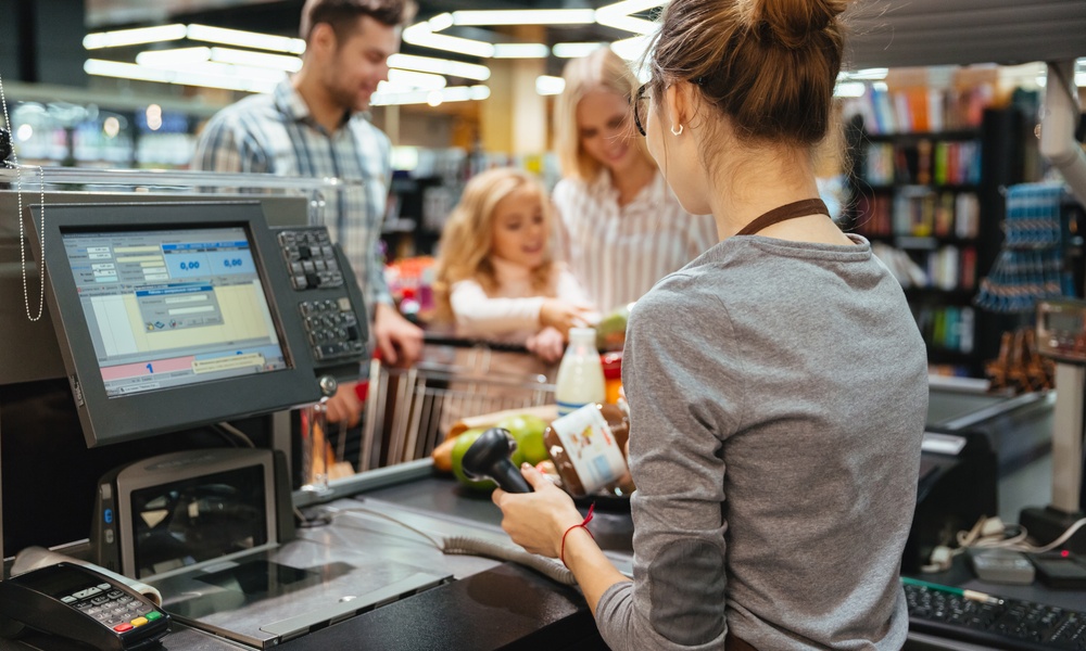 Two parents and their child stand in front of a convenience store cash register while an employee scans a product.